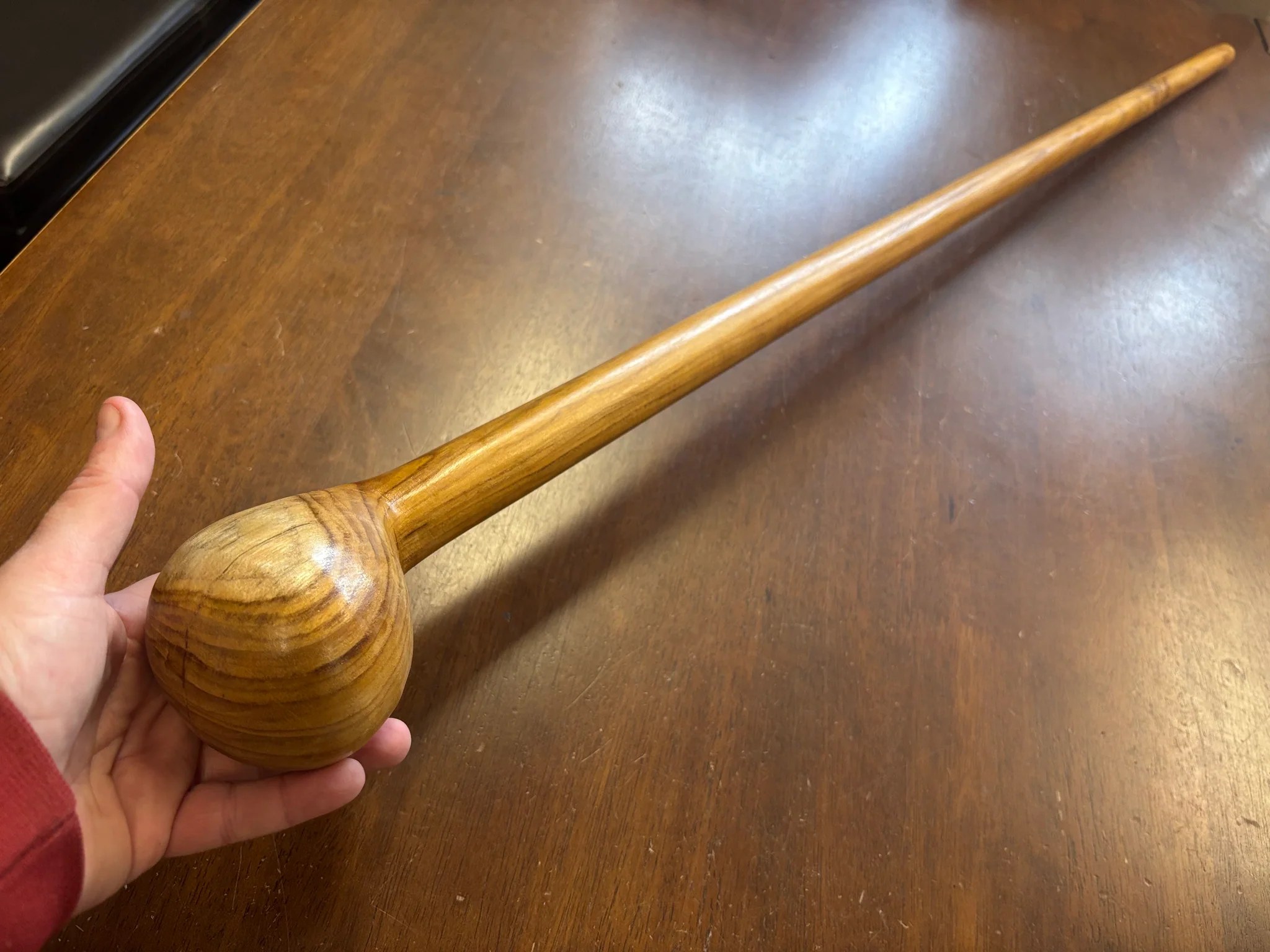 A finished oak shillelagh laid on a wood floor, with a heavy darkened knob at the head and a polished shaft showing the characteristic open grain of the wood.